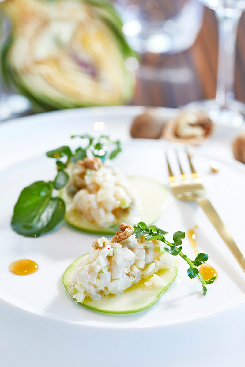 Deux quenelles de tartare de Saint-Jacques aux noix sur tranches de pomme verte, cresson et points de réduction de cidre
