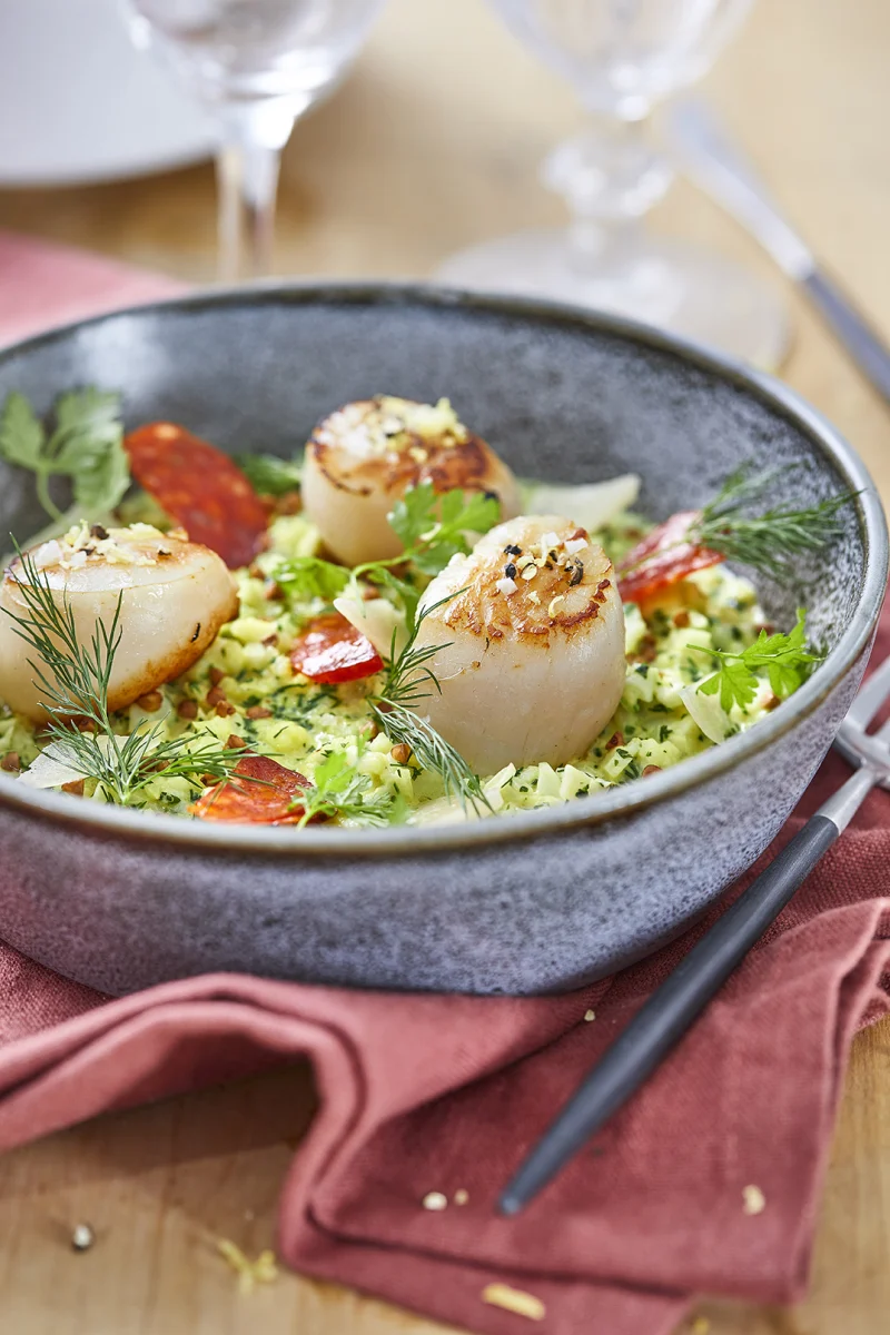 Trois noix de Saint-Jacques dorées sur un risotto de chou-fleur aux herbes, chorizo et aneth, dans un bol gris