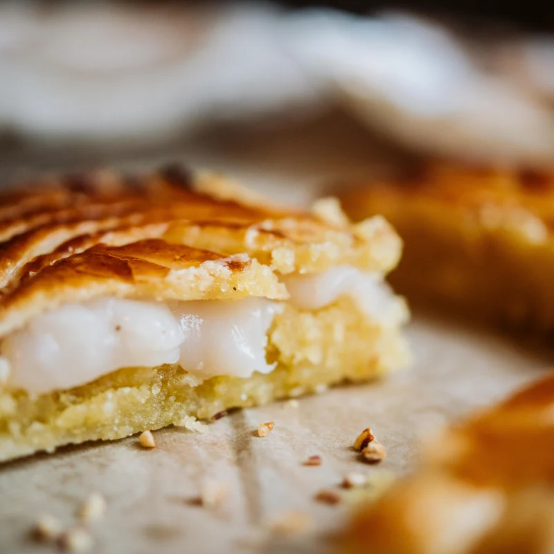 Part de galette feuilletée dorée coupée sur des demi-noix de Saint-Jacques nacrées, éclats de fruits secs sur papier
