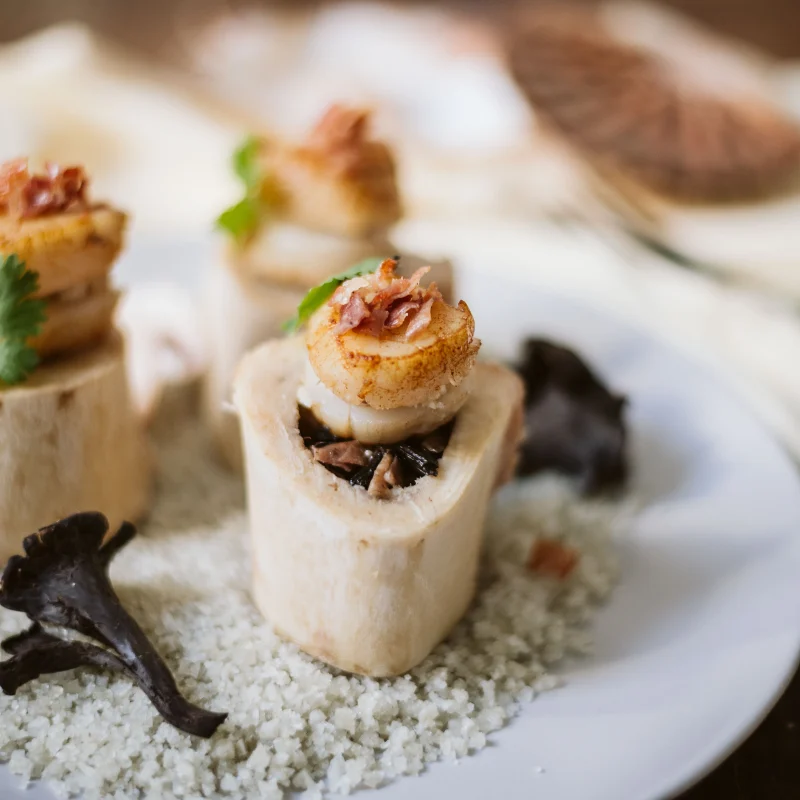 Os à moelle farcis coiffés de noix de Saint-Jacques dorées et de jambon Serrano, trompettes de la mort sur gros sel