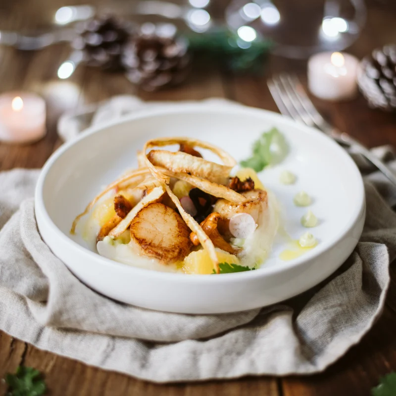 Noix de Saint-Jacques snackées sur purée de panais, girolles, suprêmes d’orange, chips de panais et points de beurre vert