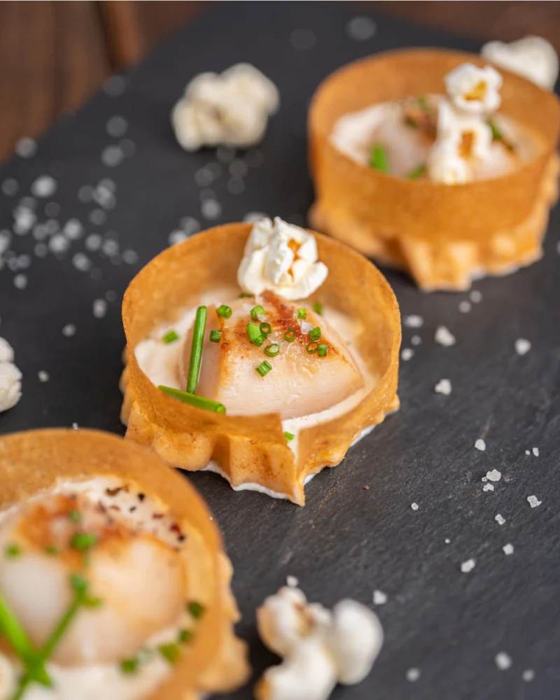 Mini croustades garnies de noix de Saint-Jacques dorées, crème et ciboulette, pop corn et fleur de sel sur ardoise