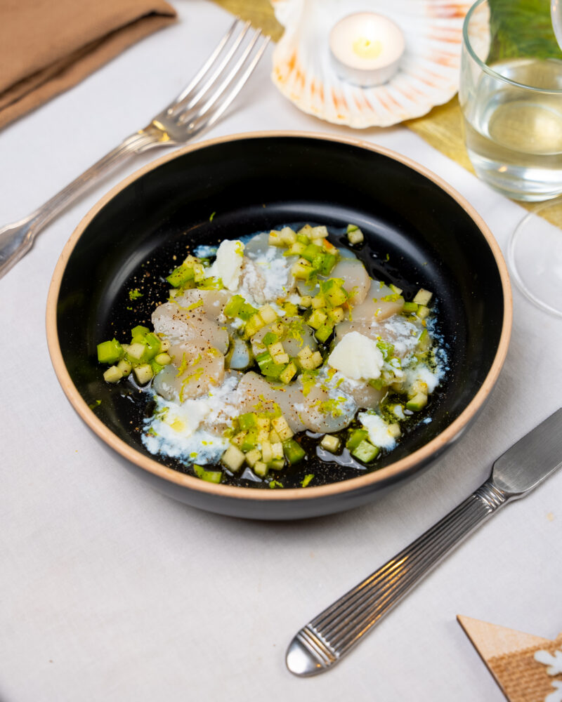 Lamelles de noix de Saint-Jacques crues, dés de céleri et de pomme verte et paillettes de granité blanc dans un bol noir