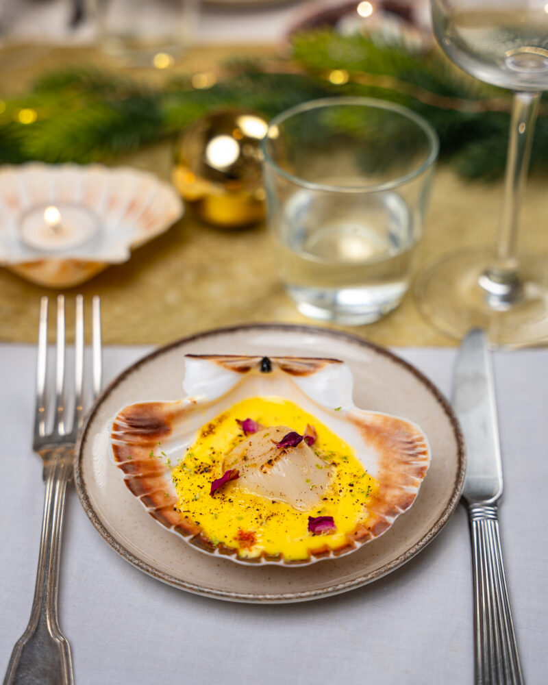 Crème safranée servie dans une coquille Saint-Jacques, noix nacrée au centre, pétales de rose et zeste vert