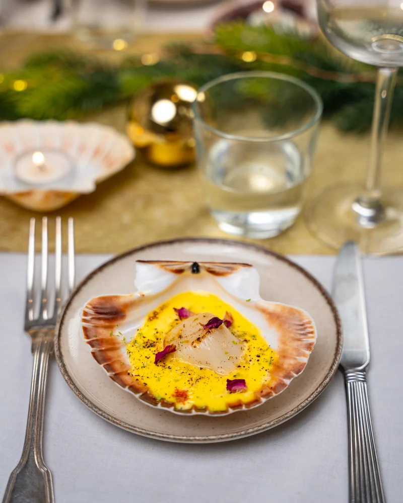 Crème safranée servie dans une coquille Saint-Jacques, noix nacrée au centre, pétales de rose et zeste vert