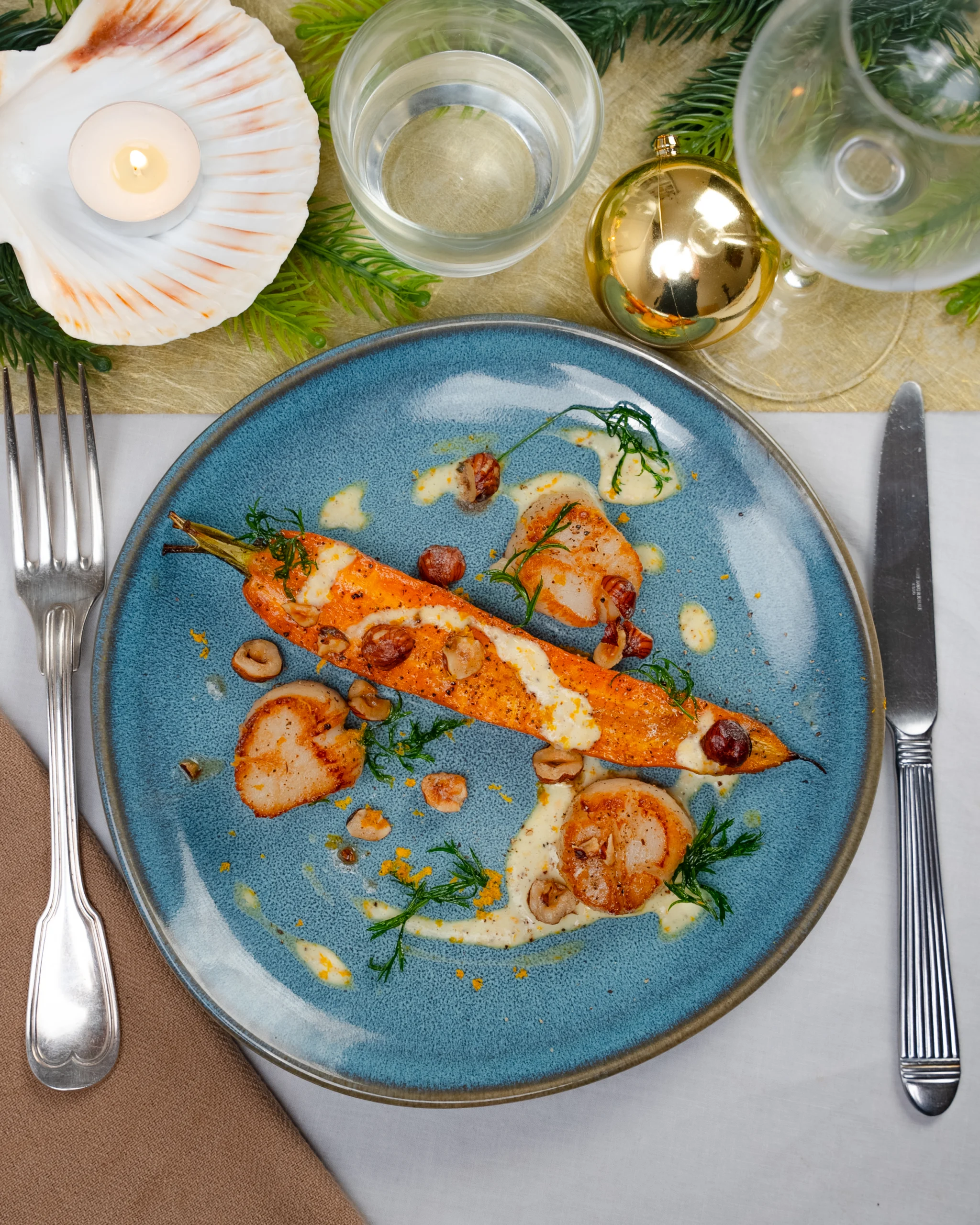 Carotte rôtie entière, trois noix de Saint-Jacques dorées, sauce crémeuse et noisettes sur une assiette bleue