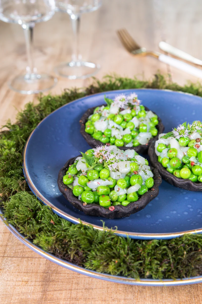 Tartelettes noires à l’encre de seiche garnies de petits pois, de cubes de noix de Saint-Jacques et de fleurs de menthe