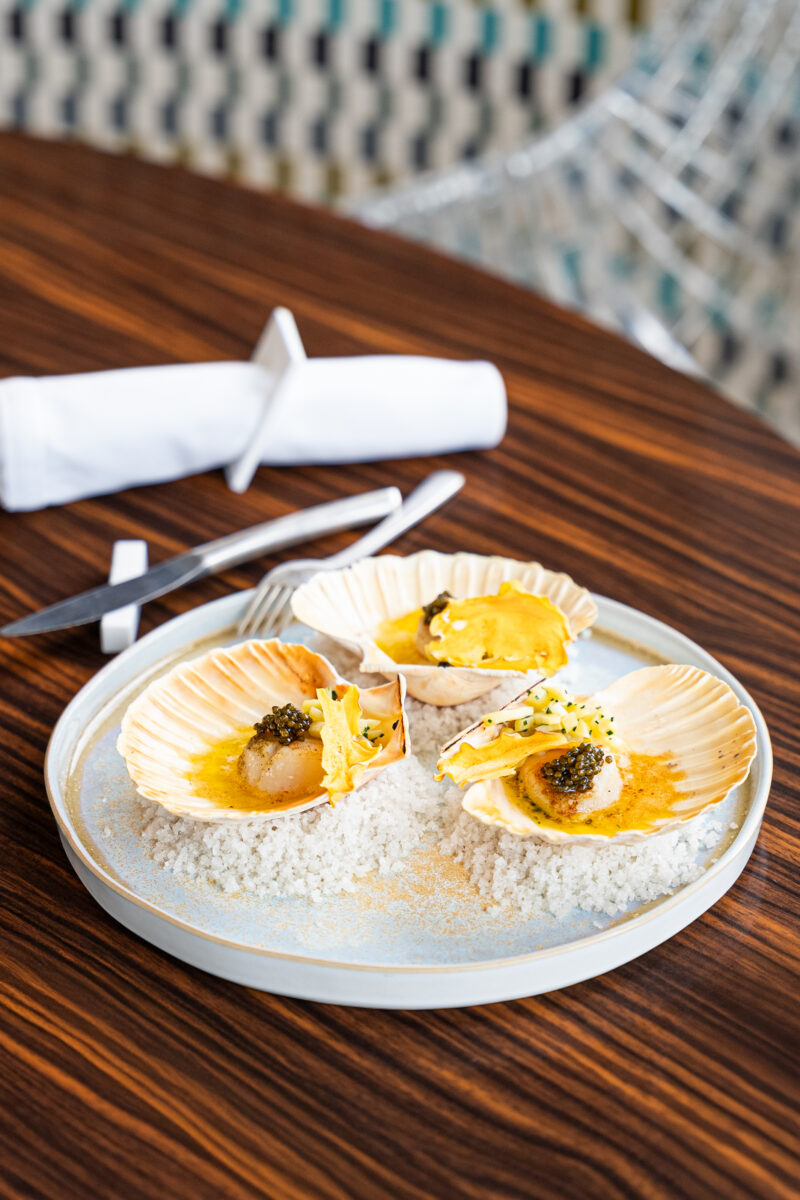 Trois coquilles Saint-Jacques sur gros sel, noix au beurre, caviar, chips et dés de panais sur une assiette bleutée