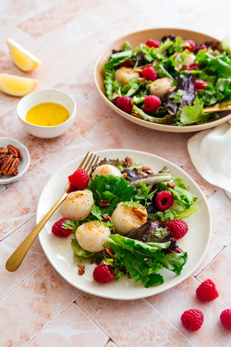 Salade de mesclun, noix de Saint-Jacques poêlées, framboises et noix de pécan dans une assiette, vinaigrette à côté