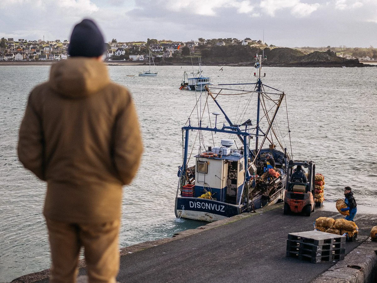 Débarquement de sacs de coquilles d'un bateau à quai, sous le regard d'un homme de dos